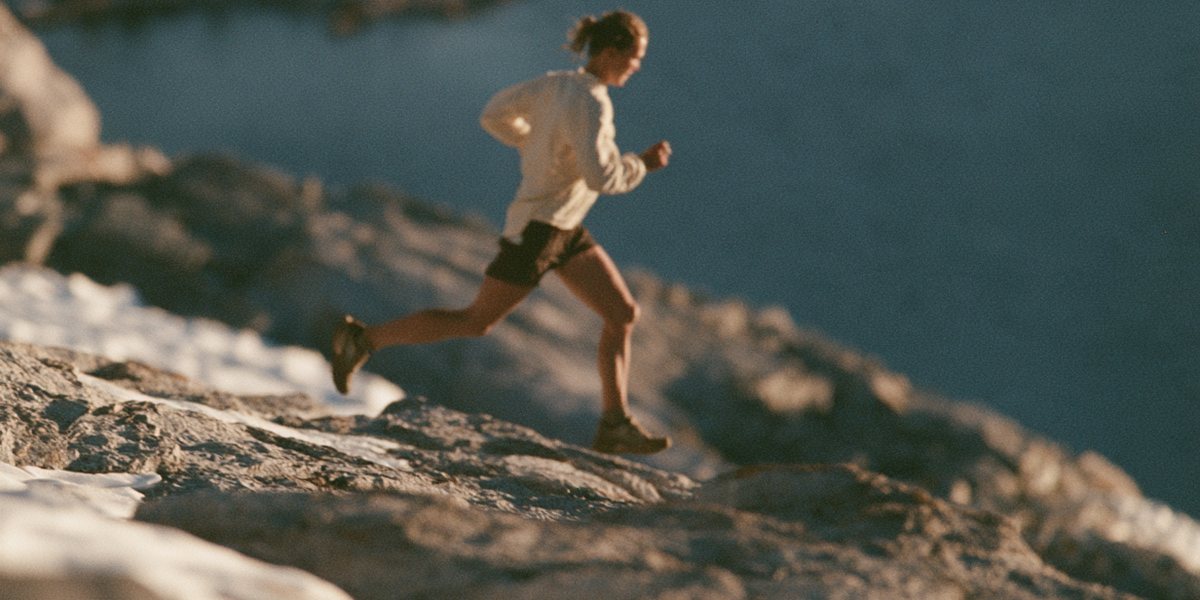 Trail runner bounding across granite and snow patches high above a deep blue lake