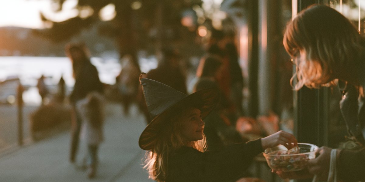 Hauntober in Tahoe City Girl in a witch hat taking candy from a shopkeeper on a lakeside sidewalk at golden hour