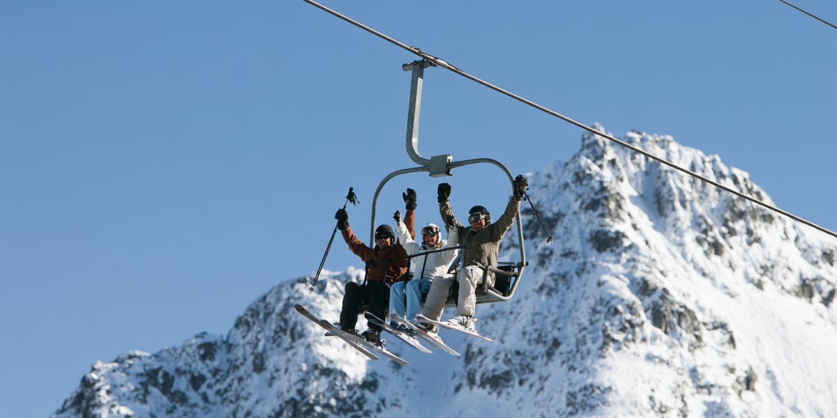 Palisades Tahoe Opening Day Friends cheering on a chairlift beneath a snowy granite peak and clear blue sky