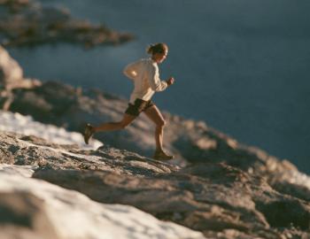Trail runner bounding across granite and snow patches high above a deep blue lake