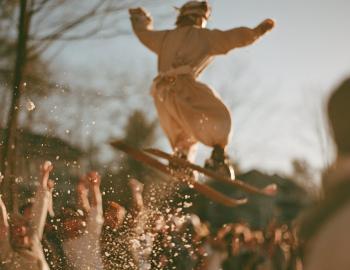 Costumed dummy on old skis flying over a cheering crowd at a spring ski event
