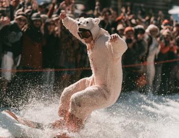 Skier in a polar bear costume splashing through a spring pond skim as the crowd cheers