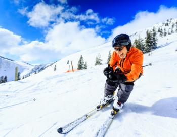 A person smiles gleefully while they ski down a groomed mountain on a clear day