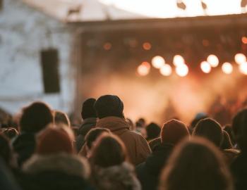 Winter concert crowd in beanies facing a warmly lit outdoor stage