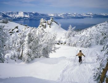 A person skis down a snowy mountain&#039;s groomed slope overlooking Lake Tahoe