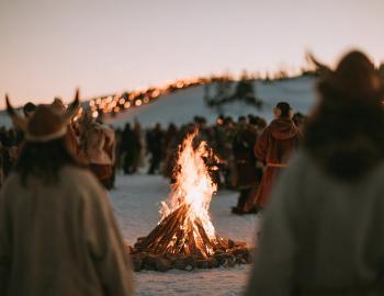 Costumed revelers in horned helmets gathered around a bonfire on the snow at dusk