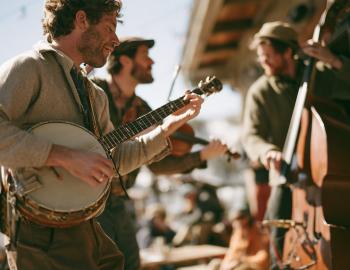 Banjo, fiddle and upright bass players performing at a sunny outdoor bluegrass festival
