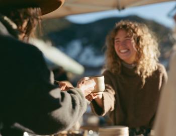 Artisan handing a handmade ceramic mug to a smiling customer at an outdoor market