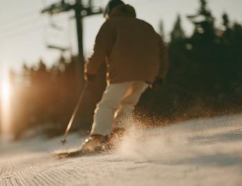 Skier carving fresh corduroy past a chairlift at sunrise, snow spraying off the edges