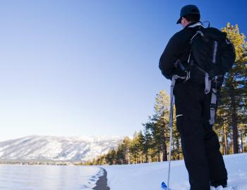 man standing still on skis or snowshoes looking at the snow