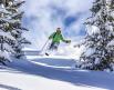 A person skis down a snowy mountain trail between trees 