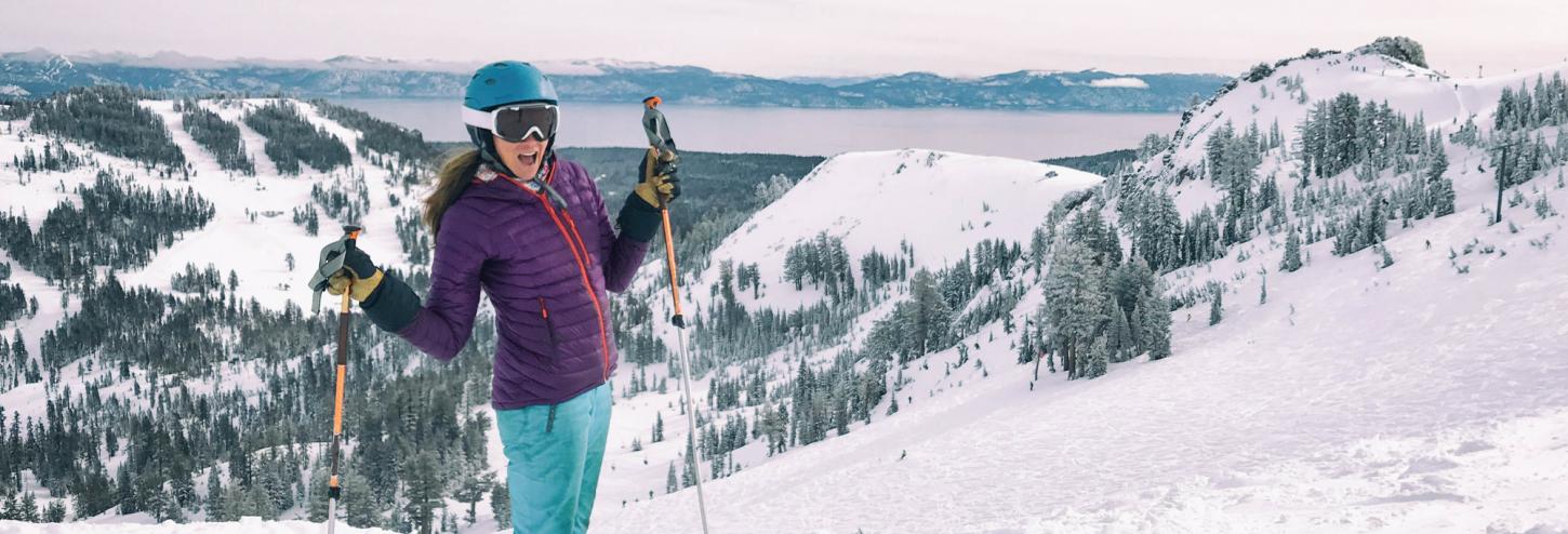 A woman poses on skis at the top of a snowy mountain