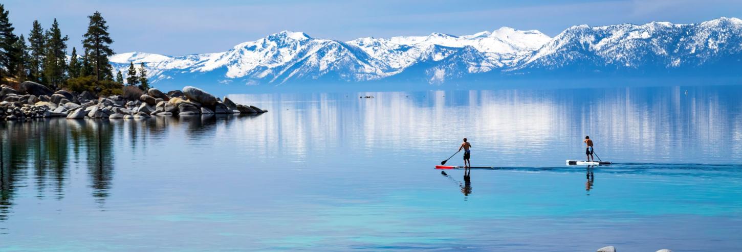 stand up paddle boarders on calm lake tahoe waters with snowy mountains in the background