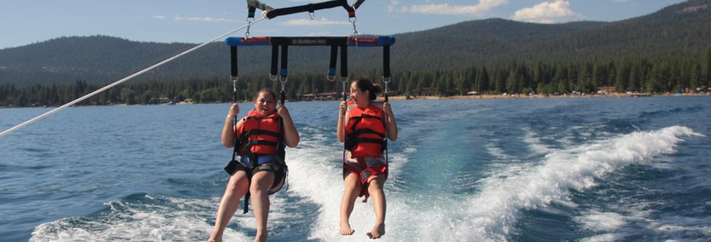 two girls parasailing behind boat feet almost touching the water