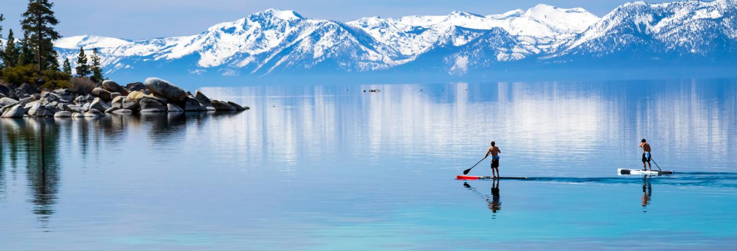 stand up paddle boarders on calm lake tahoe waters with snowy mountains in the background