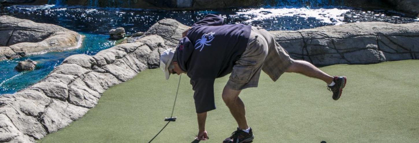 man picking up his golf ball from mini golf course