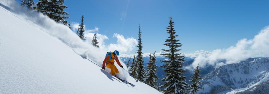 man skiing down mountain with fresh snow flying by him