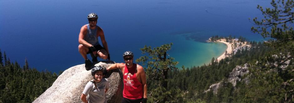 Three mountain bikers posing on rocks with lake in background