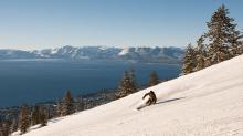 Best Ski Resorts in Lake Tahoe Skier carving a groomed run above Lake Tahoe with snow-capped Sierra peaks across the lake