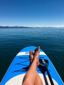 View of womens feet while sitting on paddle board in middle of the lake