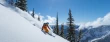 man skiing down mountain with fresh snow flying by him