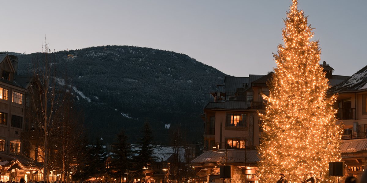 Crowd gathered around a lit Christmas tree and live band in a mountain town at dusk