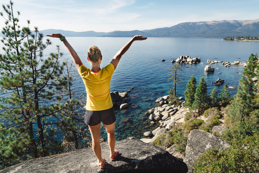 woman with arms raised after a hike by Lake Tahoe on a sunny day